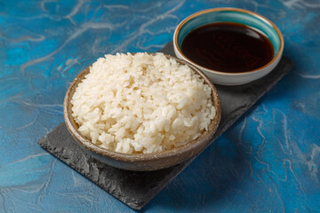 Bol de riz nature sur un plateau avec une sauje soja et baguettes. 