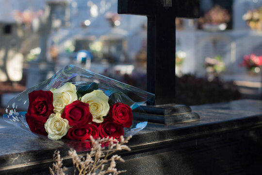 White and red roses on black granite tombstone in the open air. Funeral ceremony, all saints day or day of the dead