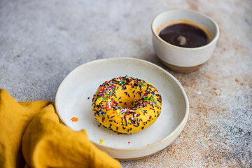 Close-up of a Banana donut with sprinkles and a cup of black coffee