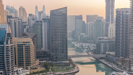 Dubai Marina with several boats and yachts parked in harbor and skyscrapers around canal aerial night to day timelapse.