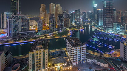 Dubai Marina with several boat and yachts parked in harbor and skyscrapers around canal aerial all night timelapse.