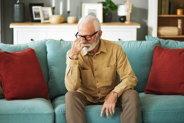 Fototapeta premium A senior man suffering from a migraine while sitting on the sofa in the living room