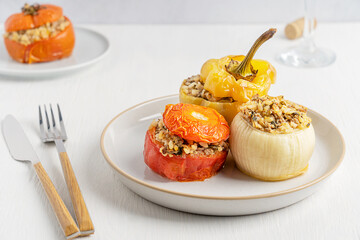 Traditional homemade vegetarian greek gemista cuisine made of pepper, onion and tomato stuffed with rice and baked until soft served on plate with tableware on white wooden table for healthy dinner
