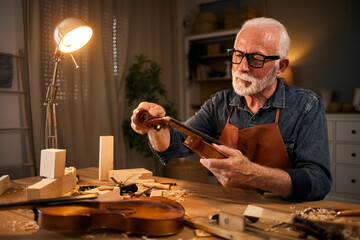 Senior carpenter craftsman carving wood and making violin instrument - obrazy, fototapety, plakaty