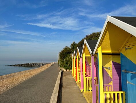 Row of multi coloured wooden beach huts on beach, Folkestone, Kent, England, UK