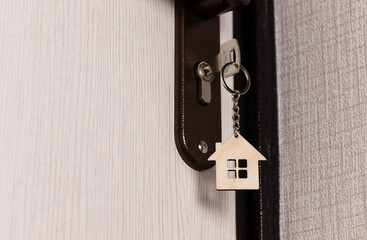 A key with a keychain in the shape of a house in the keyhole of the door