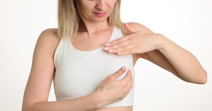 Blonde female stands on bright background carefully touching breast to relocate sore spot. Lady learns about early breast cancer diagnosis slow motion