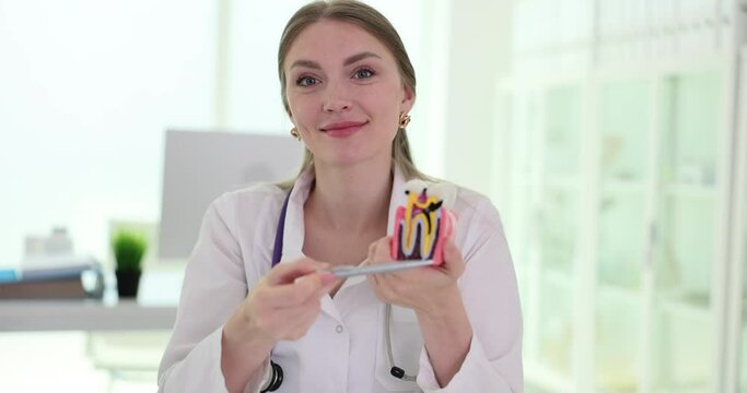 Dentist showing artificial tooth model with caries in examination room. Medical showing decayed tooth due to lack of care in clinic slow motion