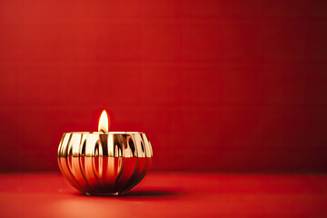 Golden mid-century candle holder with a glowing flame enhancing Christmas nostalgia isolated on a festive red gradient background  - obrazy, fototapety, plakaty