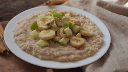 Plate of oatmeal porridge with green apple, cashew and banana. Close up.