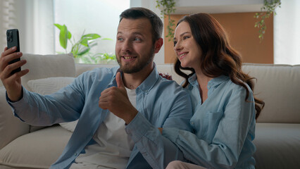 Caucasian happy couple family waving hello showing thumb up talking conversation virtual video call mobile phone conference chat blog vlog in social media bloggers speak at home with smartphone app