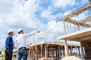 A team of two male Asian engineers, supervisors, are inspecting and pointing at a construction...