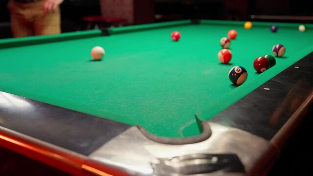 A young man plays Russian billiards, an American woman in a billiards club and bar. Dark colors in the billiard club. A man pockets snooker balls.