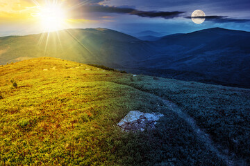 narrow path through grassy meadow among white stones on top of the hill in high mountain with sun and moon at twilight. day and night time change concept. mysterious nature scenery in morning light