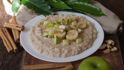 Plate of oatmeal porridge with green apple, cashew and banana. Close up.