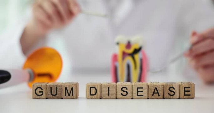 Phrase Gum Disease made of wooden cubes on white medical table against dentist with plastic model of tooth. Special treatment of gum diseases in clinic