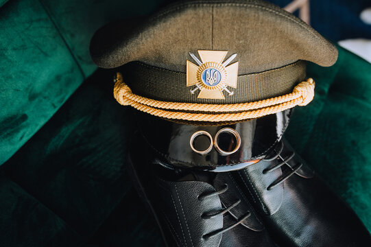 Gold rings, a cap, leather shoes, the uniform of a Ukrainian military groom on a chair. Wedding photography, accessories, details.