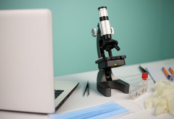 laboratory. on a white table there is a black microscope test tubes face mask medical gloves and a laptop