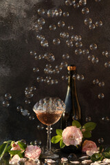 Glass of pink champagne with rose flowers on the black background with bubbles