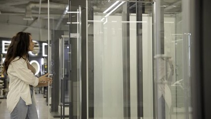 A woman examines a shower cabin before buying. The concept of renovation in the bathroom