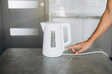 Male hands pouring water from a white electric kettle into a mug for making tea
