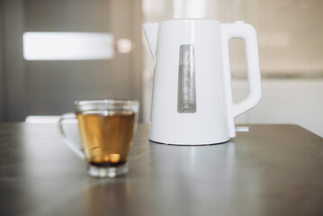 There is a white plastic teapot on the table together with a cup for brewing tea