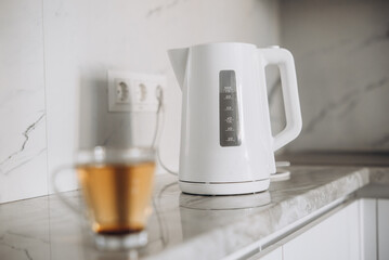 There is a white plastic teapot on the table together with a cup for brewing tea