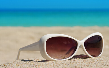 Fototapeta na wymiar White sunglasses on a sandy beach