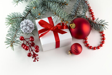 A white box with a gift tied with a red ribbon, a spruce branch and obligatory decorations on a white background