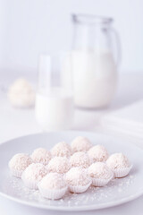 Candy with coconut flakes in selective focus. Jug and glass of milk on a white background in blur.