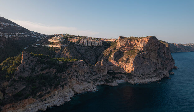 Aerial view of Breathtaking coastal panorama with clear blue sea, rugged cliffs, and the serene tranquility of small holiday houses, Cala Moraig, Zona Encinas, Cumbre del Sol, Alicante, Spain.
