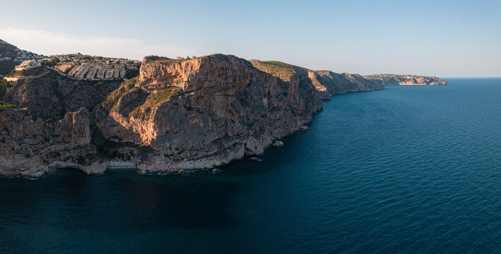 Aerial view of Breathtaking coastal panorama with clear blue sea, rugged cliffs, and the serene tranquility of small holiday houses, Cala Moraig, Zona Encinas, Cumbre del Sol, Alicante, Spain.