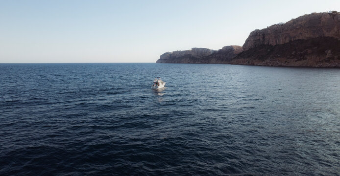 Aerial view of a small boat floating in a tranquil sea with clear blue water, Zona Encinas, Cumbre del Sol, Alicante, Spain.