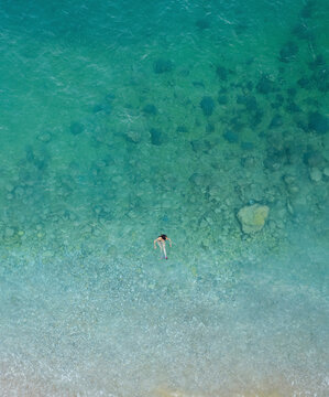 Aerial view of a woman swimming in crystal clear water illuminated by sunlight, Cala Moraig, Zona Encinas, Cumbre del Sol, Alicante, Spain.