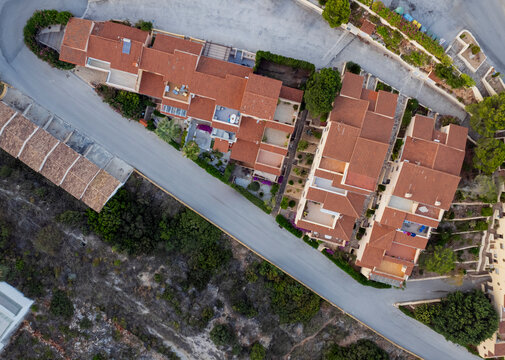 Aerial view of a lively townscape with organized architecture divided from a cliff by an asphalt road, Zona Encinas, Cumbre del Sol, Alicante, Spain.