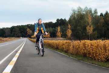 A young woman rides a bicycle in the autumn park. Cycling in the park. A healthy lifestyle in the city.