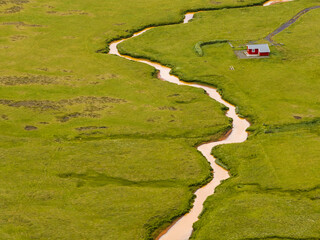 Aerial view of a small house along the river in a green grass valley, Hvolsvollur, Southern Region, Iceland.