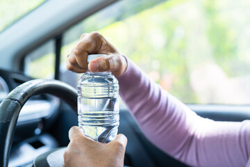 Asian woman driver holding bottle for drink water while driving a car. Plastic hot water bottle...