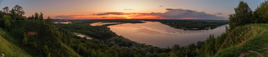 Panorama from the high bank of the river to the evening sunset over the forest.