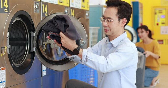 line of industrial washing machines in a public laundromat. Asian male washing clothes in automatic laundry machine