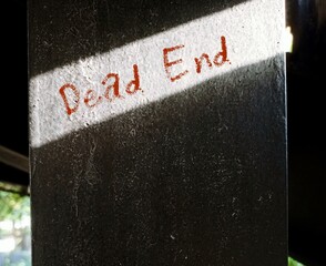 A cement post in shadow with word DEAD END, a road or path that has no way out at one end - a...