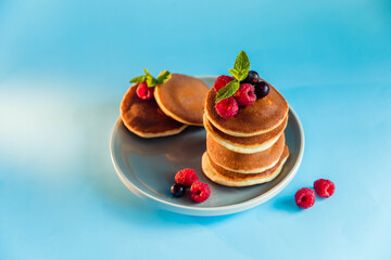 Appetizing pancakes with berries and powdered sugar on blue background