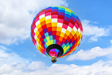 Colorful hot air balloon flying over blue sky with white clouds	