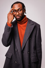 Fashionable african american man in eyeglasses, red sweater and coat looking away isolated on grey