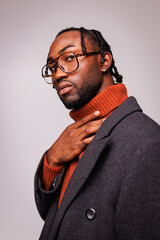 Fototapeta premium Portrait of stylish young african american man in eyeglasses, knitted sweater and coat looking at camera isolated on grey