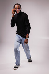 African american man in stylish eyeglasses, black turtleneck and jeans posing on grey background