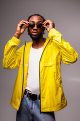 Fashionable african american man in yellow windbreaker jacket wearing sunglasses isolated on grey