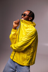 Cheerful and stylish african american man in sunglasses touching bright windbreaker jacket isolated on grey