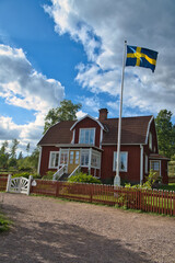 a typical red and white swedish house in smalland. White garden gate, brown fence