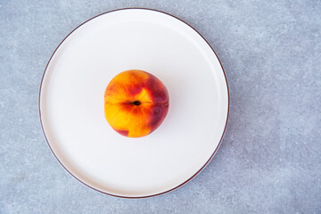 Ripe peach on a white plate on a gray background, top view